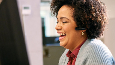 Woman wearing a headset sitting at computer desk laughing