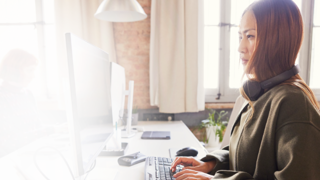 woman sitting at computer using keyboard with headphones around neck