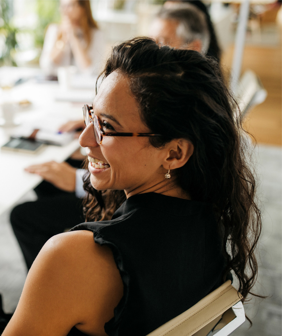 A group of people collaborating around a business table with a female prominently smiling