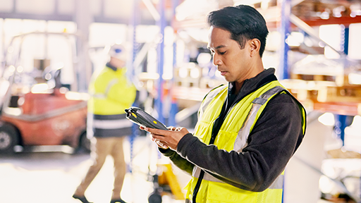 A woman in a suit giving orders to a man in high visibility gear in a warehouse setting