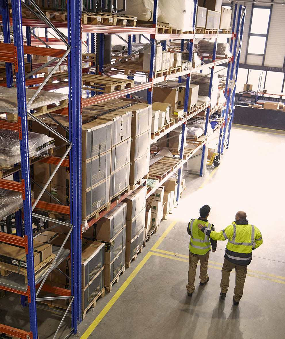 Two people in high visibility gear walking through palette racks