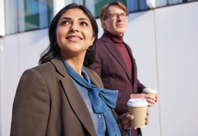 A male and female professionals co-workers walking with coffees 