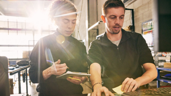 Two people at keyboard comparing notes in warehouse setting