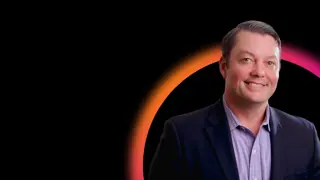 Josh Needle in front of black background with orange and pink half circle graphic