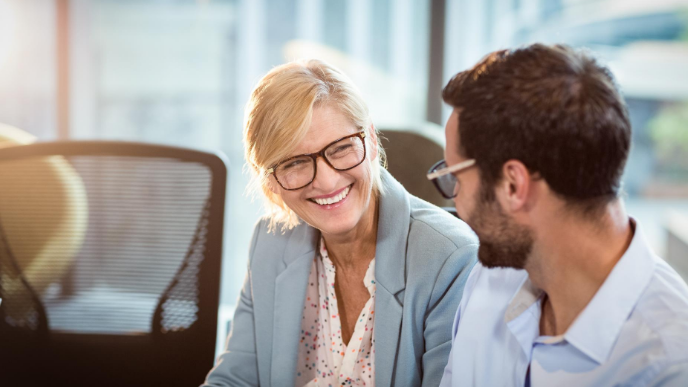 Two coworkers wearing glasses smiling and looking at each other