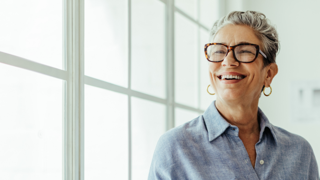 Woman with glasses smiling in front of window